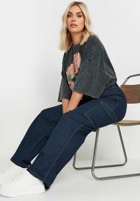 Tumman denim-tyyliset leveät cargo-housut, joissa on ommeltuja taskuja; yhdistettynä tummanharmaaseen paitaan, jossa on vaaleanpunaisia kukkia. Valkoiset tennarit viimeistelevät kokonaisuuden.