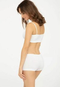 Biały bawełniany stanik i dopasowane szorty, charakteryzujące się prostym wzornictwem, cienkimi ramiączkami i gładką powierzchnią, widziane z boku z naturalnymi krzywiznami.
