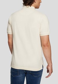 Polo shirt i beige stof med en blød tekstur, med en klassisk krave og korte ærmer, parret med blå denimbukser.