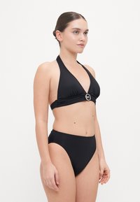 Zwart bikini-set met een halternekdesign, een driehoekige top met een metalen logo-accent en hoog aangesneden onderstukken met een soepele textuur.