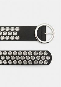 Curea din piele neagră cu o cataramă circulară din argint și grommeturi metalice distribuite uniform de-a lungul curelei. Textură netedă, formă rectangulară.