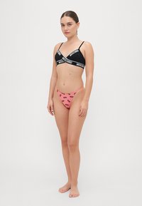 Svart bralette med hvit Moschino-logo, parret med rosa bikini-bukser med gjentatt logo-print. Glatt, elastisk stoff.