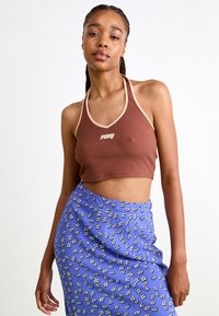 Brun ribbes halterneck crop top med beige kant; parret med et blåt blomster-mønstret nederdel med små hvide og sorte blomster.
