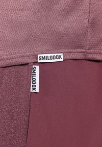 Bordové sportovní tričko s texturovanou, prodyšnou tkaninou. Má jednobarevný design a výrazné štítky "SMILODOX" našité na materiálu.