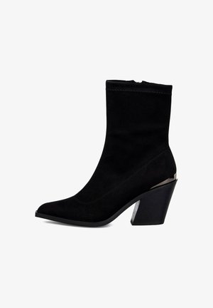 Bottine en suède noir avec un embout pointu, dotée d'un talon épais avec des accents métalliques, texture lisse et design sans couture.