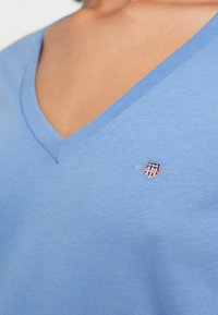 Jasnoniebieska koszulka z dekoltem w serek wykonana z bawełny, z haftowanym logo na piersi. Miękka w dotyku i o casualowym designie.