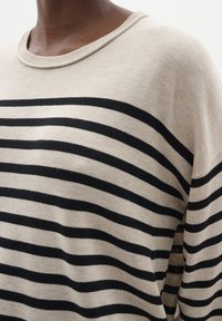 Maglione a maglia beige con ampie strisce nere, scollo rotondo e vestibilità morbida. La trama sembra morbida con dettagli di cucitura visibili.