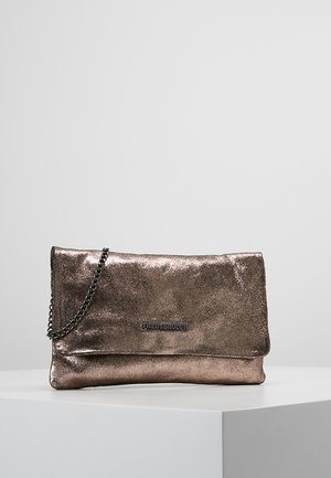 Pochette en bronze métallique avec bandoulière chaîne et rabat pliant, posée sur une surface blanche sur fond gris uni.