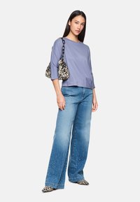 Helles blaues, leichtes Oberteil mit 3/4-Ärmeln, kombiniert mit weit geschnittenen, hellblauen Jeans, akzentuiert mit Strasssteinen und einer Handtasche mit schwarz-beigem Leopardenmuster.