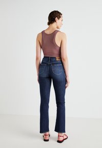 Uitgebrede donkerblauwe jeans met contrasterende stiksels en een leren label op de tailleband, gecombineerd met een aansluitend, geribd mauve tanktop.