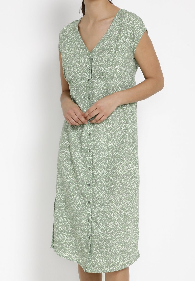 Robe à imprimé floral vert avec de courtes manches courtes, décolleté en V et fermeture à boutons sur le devant ; elle présente une coupe décontractée et des fentes sur les côtés.