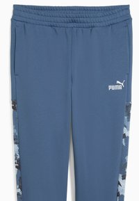 Blå Puma joggingbukser med elastisk talje, sidelommer og mønstrede paneler, som løber ned ad ydersiden af benene. Puma-logo i hvidt på venstre lår.