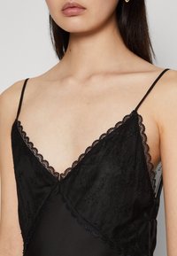 Camisole noire avec un délicat bord en dentelle, des bretelles spaghetti réglables et une texture lisse semblable à du satin, avec un décolleté en V.