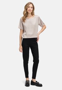 Lichtbeige satijnen top met korte mouwen, gecombineerd met zwarte slim-fit broek en glanzende zwarte loafers, met een zachte textuur en een eenvoudig ontwerp.