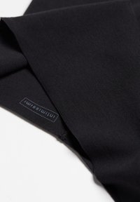 Černá látka s hladkým povrchem, na které je malá modrá etiketa se značkou. Látka je složená a ukazuje čistý okraj.