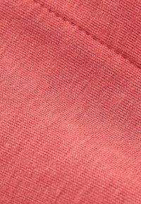 Tessuto in corallo rosa, caratterizzato da una trama testurizzata con cuciture visibili. Il tessuto appare morbido e leggero, con un colore uniforme.