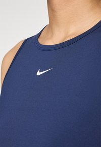 Mørkeblå ermeløs treningstopp med rund hals, laget av glatt, elastisk stoff. Har en hvit Nike-logo på brystet.