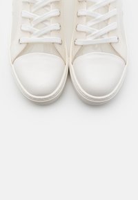 Pár bílých tenisek se šňůrkami, zobrazených z horního pohledu se zaměřením na špičky a přední části na bílém pozadí.