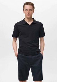 Svart polo t-shirt med platt krage och korta ärmar, kombinerad med m�örka shorts. Tyget verkar slätt och lätt, lämpligt för avslappnad användning.