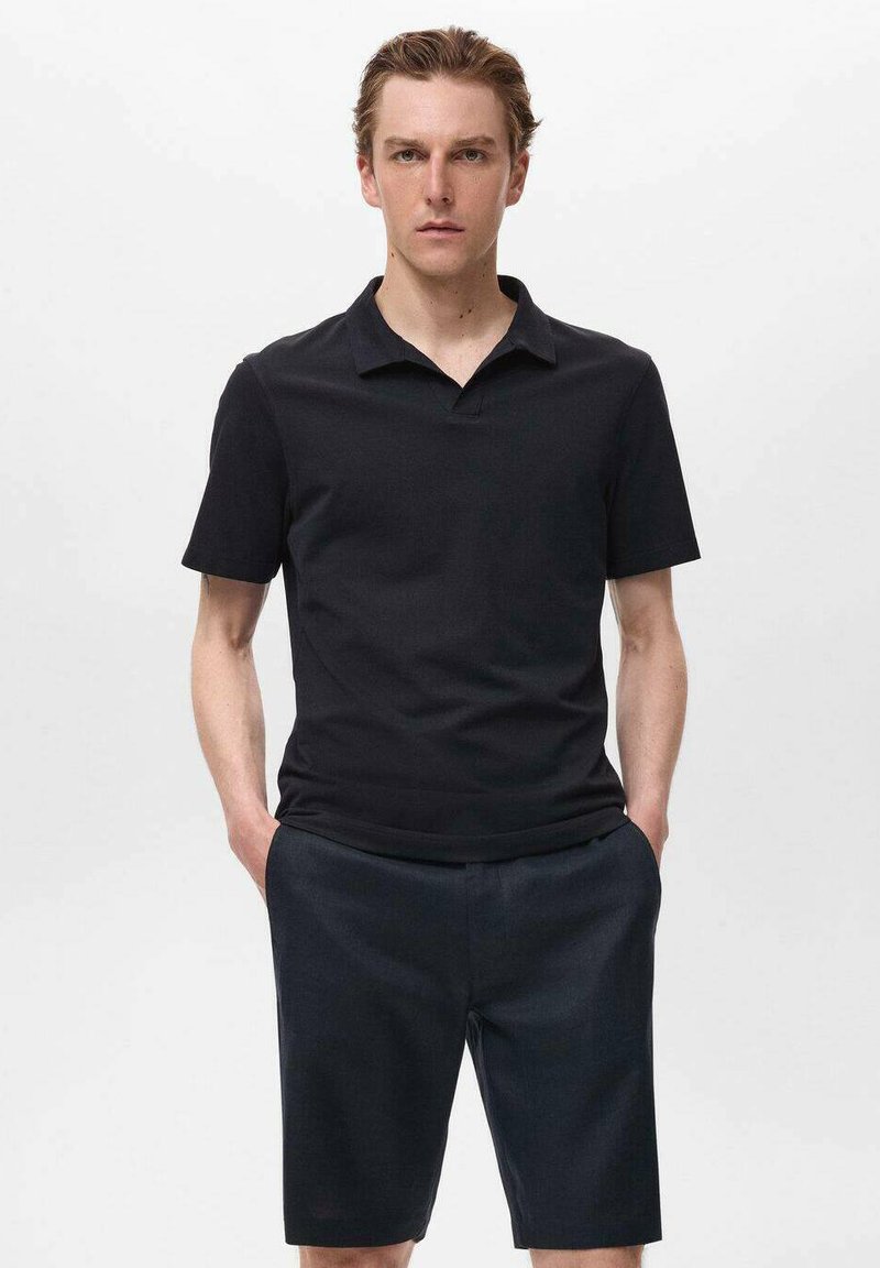 Svart polo t-shirt med platt krage och korta ärmar, kombinerad med mörka shorts. Tyget verkar slätt och lätt, lämpligt för avslappnad användning.