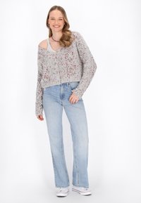 Maglione a maniche lunghe grigio chiaro, tagliato, con un motivo a macchie, abbinato a jeans svasati azzurri e sneakers bianche. Tessuto liscio, vestibilità rilassata.