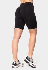 Pantaloni sportivi neri realizzati in tessuto elasticizzato, caratterizzati da un design aderente e che arrivano a metà coscia, abbinati a scarpe da corsa grigie e nere.