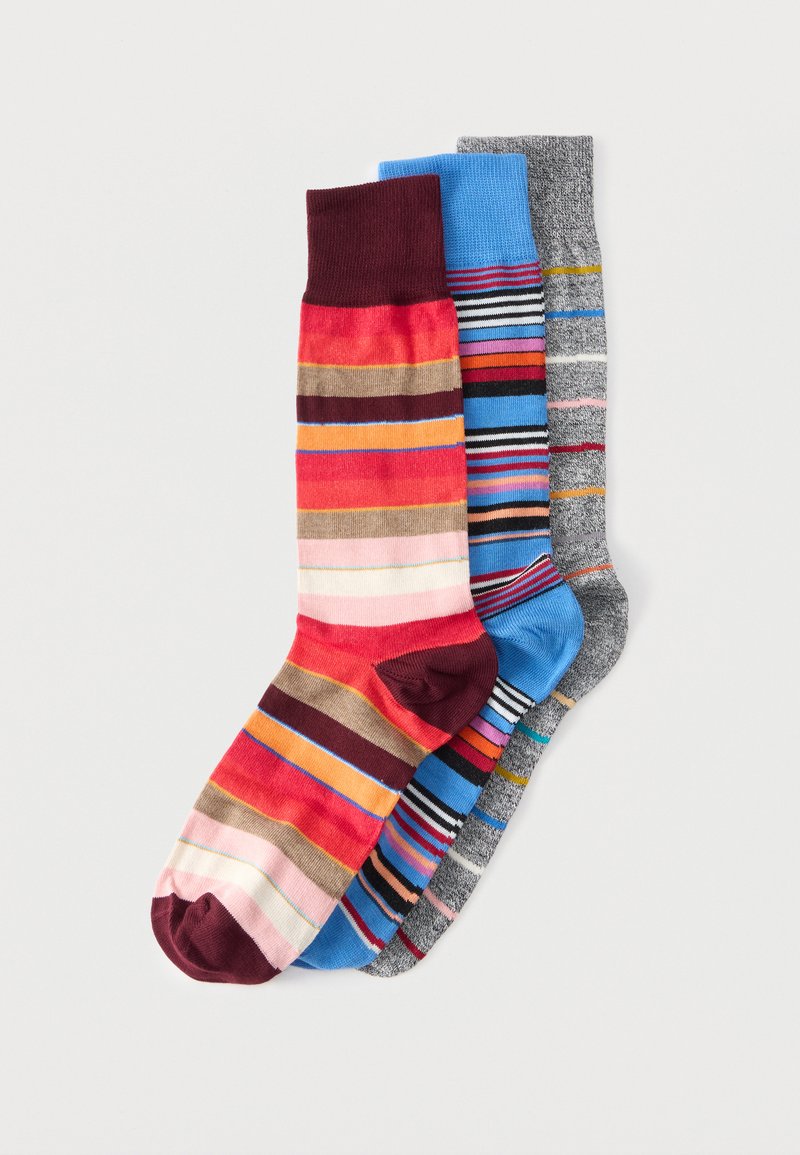 Trois paires de chaussettes rayées colorées, une ton rouge, une ton bleu et une ton gris, disposées en chevauchement sur un fond blanc.