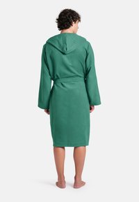 Accappatoio verde con cappuccio realizzato in un tessuto morbido e assorbente. Presenta maniche lunghe, una cintura da annodare e un taglio fino al ginocchio con una texture liscia.