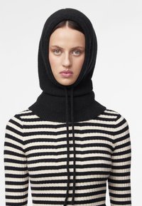 Cappuccio nero lavorato a maglia con texture a coste, dotato di coulisse, abbinato a un maglione a righe bianche e nere.
