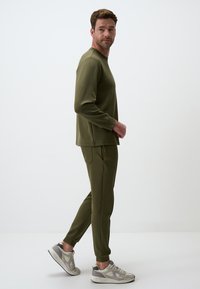 Olive green sweatshirt and joggers, both in a soft fabric. The top features a crew neck; the pants have side pockets and tapered cuffs. Sneakers complete the look.