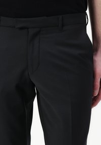 Maßgeschneiderte schwarze Hosen aus glattem Stoff, mit schmaler Passform, flachem Bund, seitlichen Taschen und dezenten Nähten.
