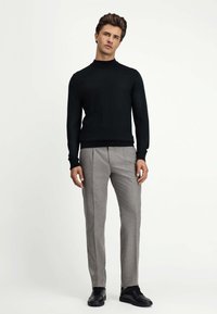 Czarny dopasowany sweter z wysokim kołnierzem, zestawiony z jasnoszarymi, szytymi na miarę spodniami. Całość dopełniają czarne sneakersy. Minimalistyczny design.
