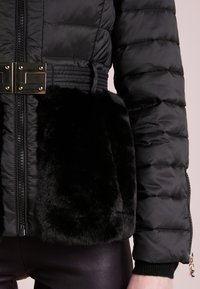 Czarna kurtka puchowa z pikowaną fakturą, kieszeń z akcentem z sztucznego futra, złote okucie z klamrą, zamek błyskawiczny oraz ribbowe wykończenie mankietów.
