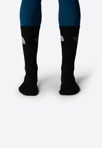 Calcetines negros de punto con textura acanalada, que presentan un diseño de logotipo blanco en el puño. Los calcetines son de longitud hasta el tobillo, con un ajuste ceñido.