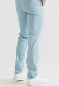 Pantalons en coton bleu clair avec une coupe ajustée, poches latérales et texture lisse, associés à des baskets blanches.