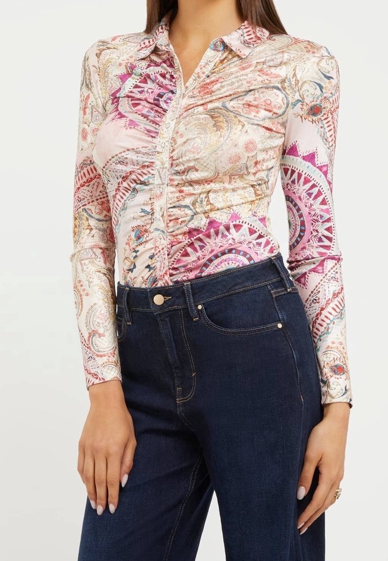 Femme portant une chemise à manches longues boutonnée avec des motifs cachemire roses et beiges, associée à un jean bleu foncé taille haute.