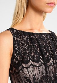 Robe en dentelle noire avec des motifs floraux intriqués, une conception sans manches et un ourlet festonné. Superposition transparente avec une doublure douce.