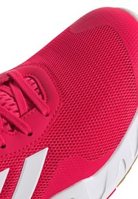 Heldere roze sportieve schoen met een mesh bovenwerk, een gestructureerd ontwerp, tonale veters en een witte rubberen zool met een kenmerkend golfpatroon.