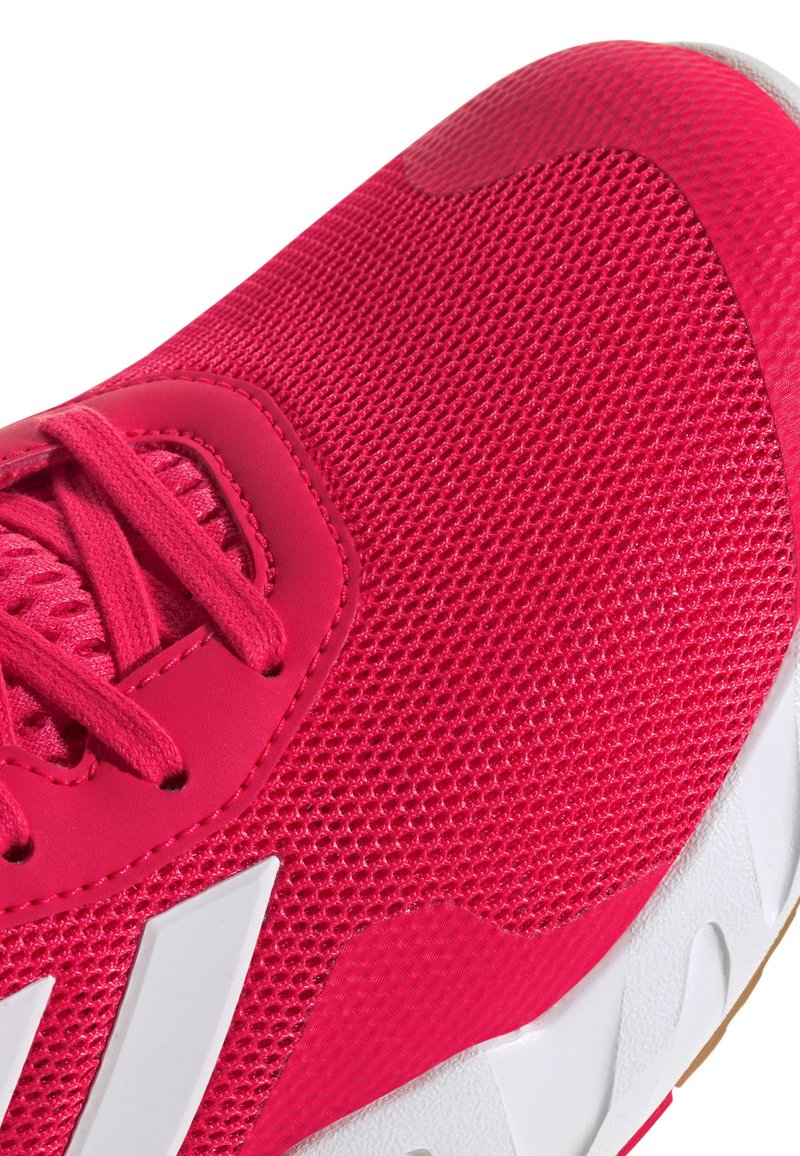 Chaussure de sport rose vif présentant une tige en maille, un design texturé, des lacets ton sur ton et une semelle en caoutchouc blanche avec un motif de vagues distinctif.
