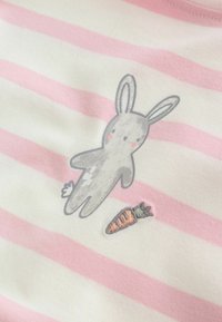 Tissu rayé rose et blanc avec une illustration de lapin gris et une petite carotte brodée près de ses pattes.