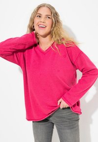 Sudadera rosa con escote en V, patrón de estrellas y mangas largas, combinada con jeans grises. El material parece suave y texturizado.