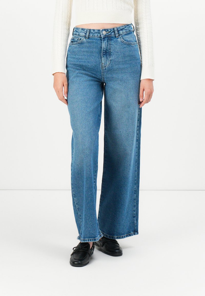 Brett blå denimjeans med hög midja, har bältesöglor och stängning med framknapp. Materialet har en lätt blekning och slät textur.