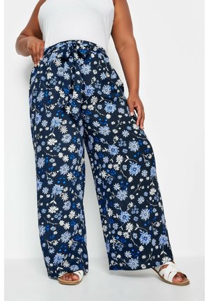 Pantalons larges à fleurs marines avec des fleurs bleues et blanches. Détail de taille nouée et tissu léger. Associés à des sandales blanches.