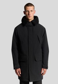 Svart parkas med en stor, texturerad krage, två framfickor och rak passform. Materialet verkar slätt och hållbart.