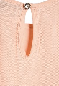 Persikofärgad topp i ett strukturerat mesh-material, med en nyckelhålöppning på baksidan som hålls på plats med en matchande knapp.