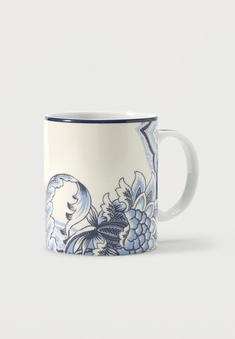 Tasse en céramique blanche avec des motifs floraux et cachemire bleus et un bord marine, présentée sur un fond clair uni.
