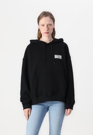 Black hoodie, cotton material, oversized design with a kangaroo pocket, drawstring hood, and a small white logo on the chest.