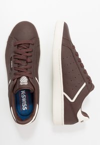 Baskets en cuir marron avec surface texturée, bout rond et accents perforés. Dotées de lacets marron foncé et d'une semelle extérieure en caoutchouc blanc.