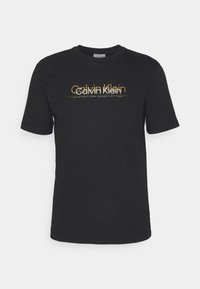 Black cotton t-shirt featuring short sleeves and a crew neck. Front design includes "Calvin Klein" in gold and white typography.