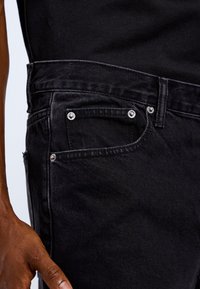 Czarne dżinsy z denimu o dopasowanym kroju, srebrnymi elementami i małą kieszonką. Faktura jest gładka z lekkim połyskiem.